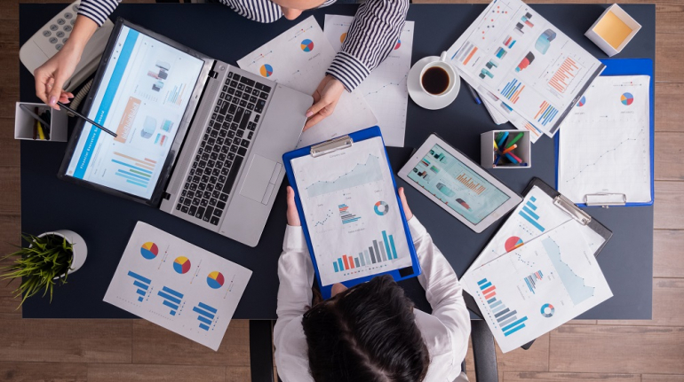 Top viewTop view of manager and employee doing teamwork in business office , looking at charts on laptop display. Finance paperwork with charts at workplace. Discusing financial plan.